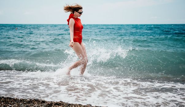 Young happy woman walks carefree on the seaside. Happy lady in red bikini. Portrait beautiful young woman relax smile around beach sea ocean in holiday vacation travel trip.