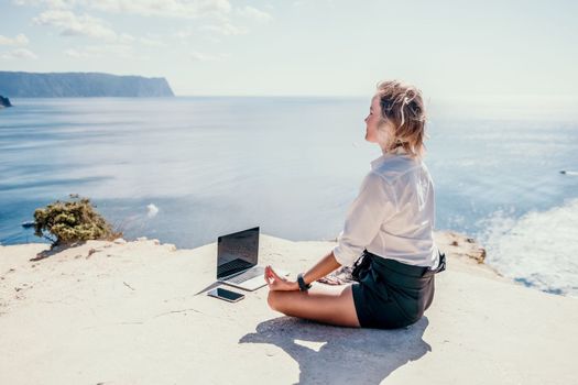 Happy girl doing yoga with laptop working at the beach. beautiful and calm business woman sitting with a laptop in a summer cafe in the lotus position meditating and relaxing. freelance girl remote work beach paradise