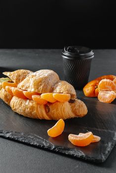 croissant with mandarins sweet on a dark background. Homemade croissants. Falling powdered sugar. Vertical