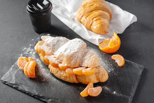 Sweet croissant sandwich with powdered sugar on a dark background. Baking and bakery concept.