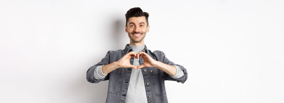 Handsome man showing heart gesture and smiling. Romantic guy say I love you and smiling tender at camera. Valentines day concept.