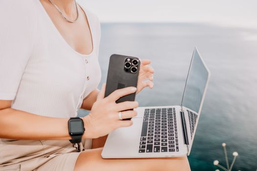 Digital nomad, Business woman working on laptop by the sea. Pretty lady typing on computer by the sea at sunset, makes a business transaction online from a distance. Freelance remote work on vacation