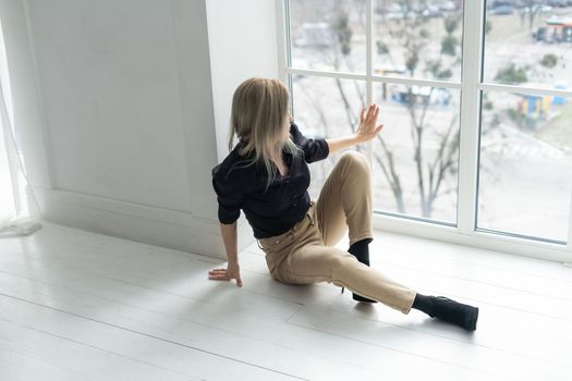 Side view of young businesswoman in white shirt sitting on floor near window.