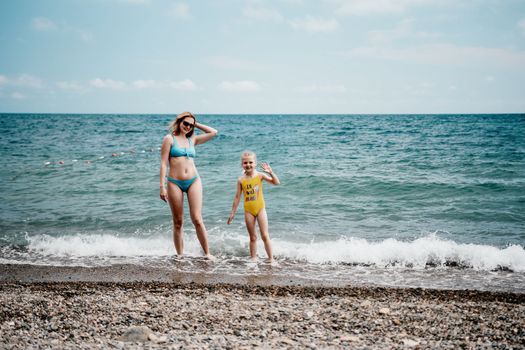 Happy loving family mother and daughter having fun together on the beach. Mum playing with her kid in holiday vacation next to the ocean - Family lifestyle and love concept.