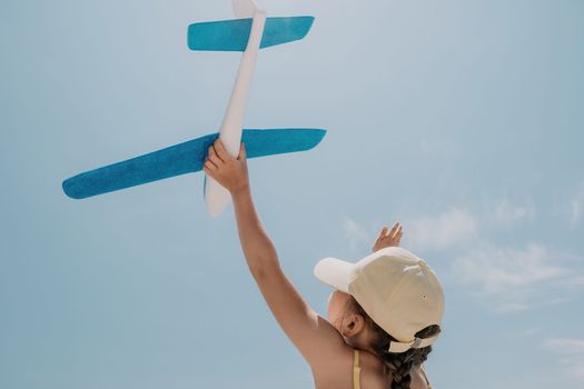 Kid playing with toy airplane. Children dream of travel by plane. Happy child girl has fun in summer vacation by sea and mountains. Outdoors activities at background of blue sky. Lifestyle moment