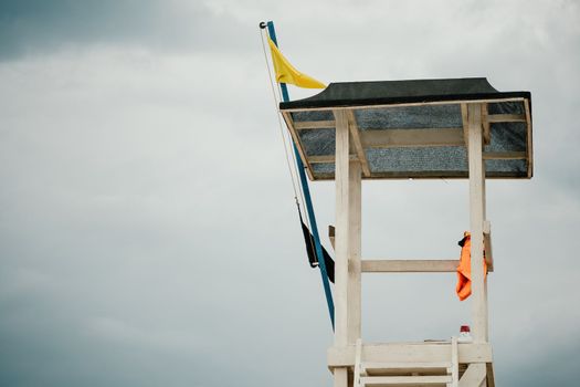 Empty white lifeguard tower with a yellow flag on the beach in windy weather. Beach lifeguard tower with yellow flag indicator. Nobody. Holiday recreation concept