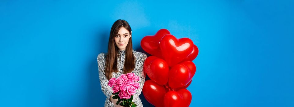 Valentines day. Pretty woman making romantic gift to girlfriend, stretch out hands with beautiful pink flowers and smiling, standing on blue background.