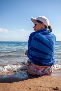 A beautiful girl in a swimsuit with long hair and a white cap looks at the blue sea. Rear view.