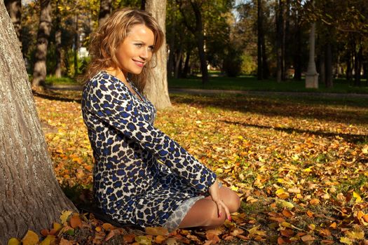 woman sit and smile on ground near tree in autumn leaves