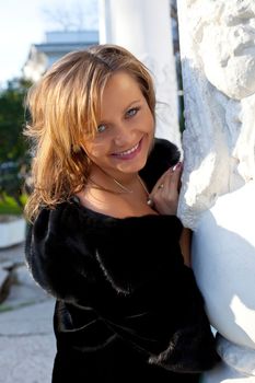 Beauty woman near column in fur coat smile