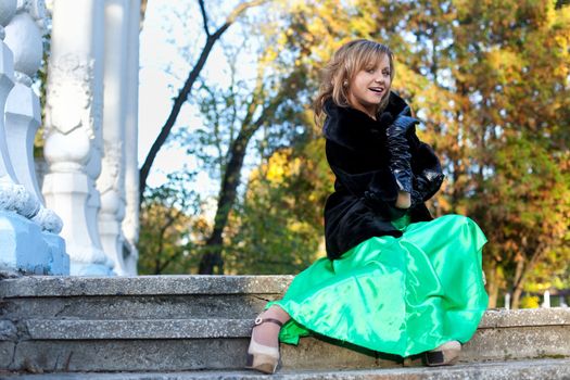 Beauty woman in green clothes and fur coat sit on stairs