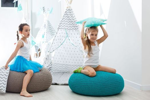 Stay Home Stay Safe. Two happy kids sitting on cozy chair relaxing playing in white living room indoors. Sisters having fun at home