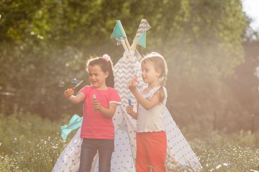 childhood and hygge concept - happy little girls playing in kids tent.
