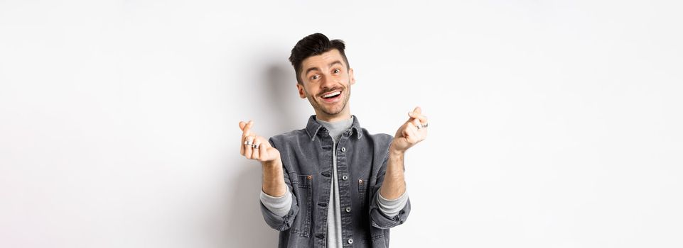 Handsome smiling man showing hand hearts and looking with love at camera, standing on white background.