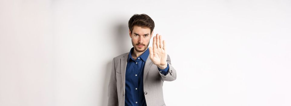 Hold right there. Serious businessman in suit stretch out hand and tell to stop, frowning and look confident, disapprove action, prohibit something bad, standing on white background.