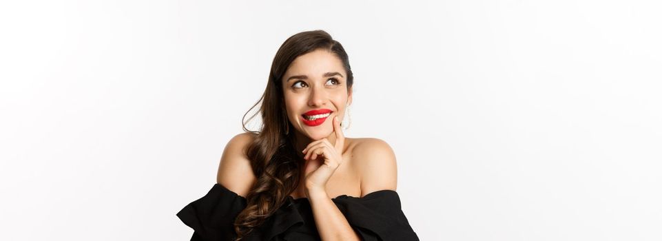 Fashion and beauty concept. Close-up of beautiful dreamy woman with red lips, looking at upper left corner and smiling tempted, having idea, standing over white background.