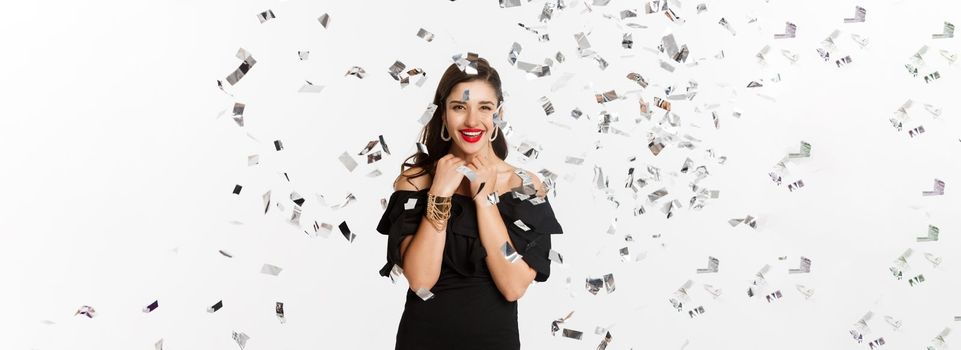 Happy woman celebrating winter holidays, smiling cheerful, partying on New Year with confetti, standing over white background.