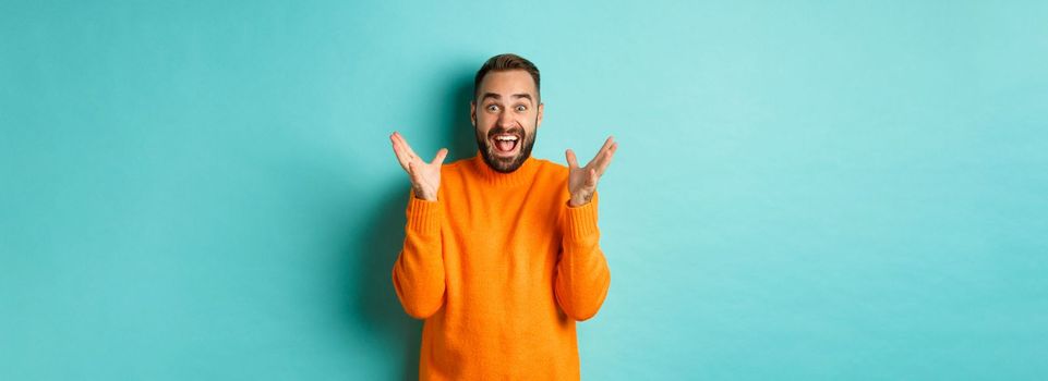 Image of excited and happy bearded man, shaking hands and smiling amazed, telling big news, standing over light blue background.