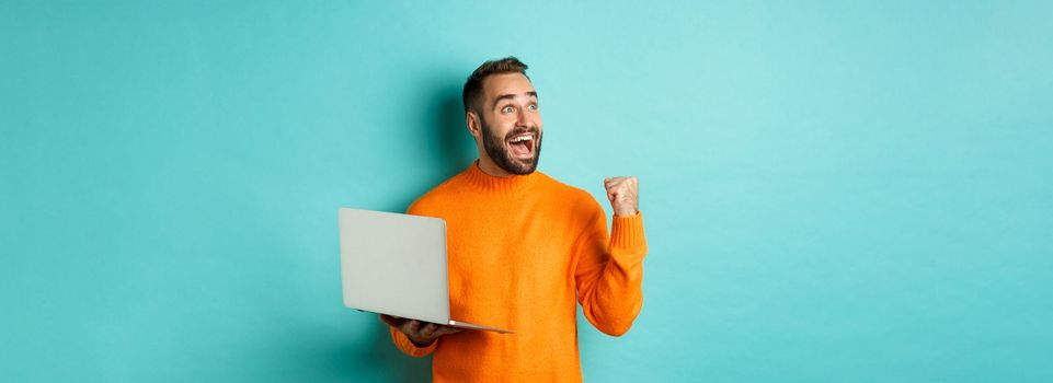 Freelance and technology concept. Lucky man winner celebrating, winning online, showing fist pump and holding laptop, looking at upper left corner.