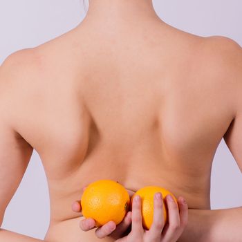 Slim woman is holding orange. Perfect female back without any cellulite.