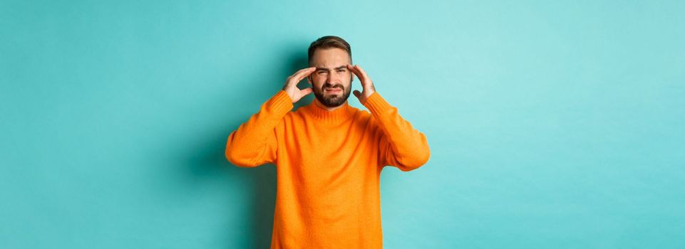 Phoro of caucasian man touching head, feeling sick, have headache or migraine, hangover after party, standing over light blue background.