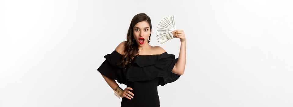 Beauty and shopping concept. Fashionable woman with red lips, showing dollars and smiling, standing over white background with money.