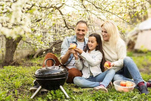 Happy girl, father and mother preparing barbecue in the yard.