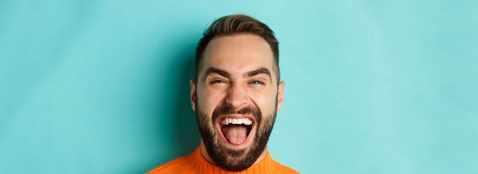 Headshot of happy and carefree man with beard, laughing and looking at camera, standing in orange sweater.