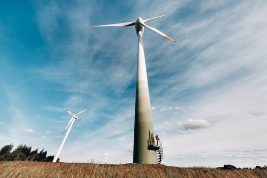 A man in a business suit with a green Golf shirt stands next to a windmill against the background of the field and the blue sky.Businessman near the windmills.Modern concept of the future