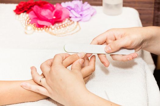 The beautician polish the client's nails before putting nail polish