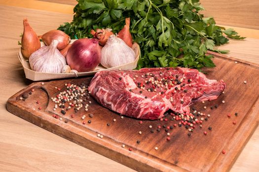 steak of beef on a wooden board with spices pepper parsley salt onions shallots garlic