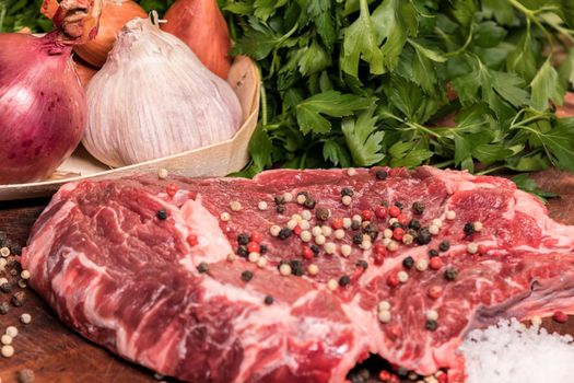 steak of beef on a wooden board with spices pepper parsley salt onions shallots garlic