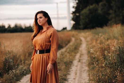 portrait of a Girl in a orangelong dress with long hair in nature in the evening