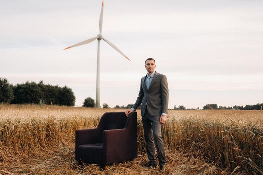 Portrait of a businessman in a gray suit and tie, standing near a chair in a wheat field.Europe.