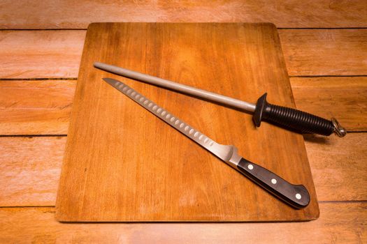 wooden cutting board with a ham or salmon knife and a sharpening gun.