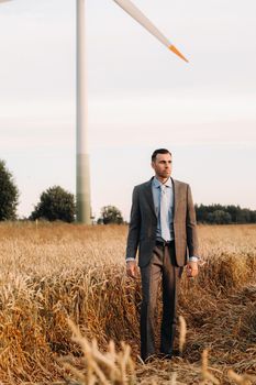 Portrait of a businessman in a gray suit on a wheat field against the background of a windmill and the evening sky.