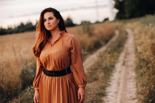 portrait of a Girl in a orangelong dress with long hair in nature in the evening