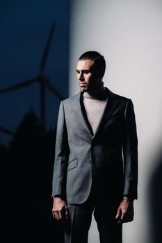 A man in a grey business suit stands next to a windmill after sunset .Businessman near windmills at night.Modern concept of the future