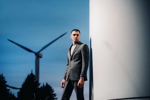 A man in a grey business suit stands next to a windmill after sunset .Businessman near windmills at night.Modern concept of the future