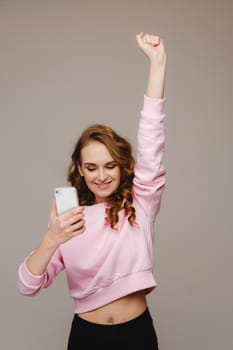 A happy young girl holds the phone looks into it and smiles holding her hand up.