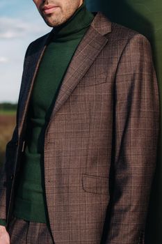 A man in a business suit with a green Golf shirt stands next to a windmill against the background of the field and the blue sky.Businessman near the windmills.Modern concept of the future.