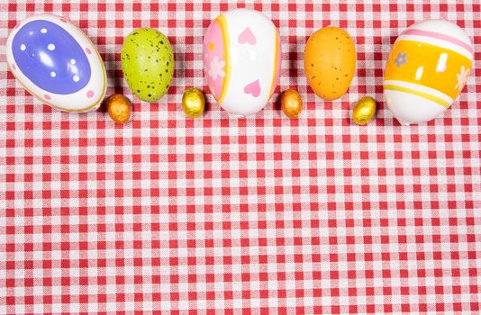 Mix of easter eggs of all colors and sizes on a background of red and white gingham fabric. Easter concept.