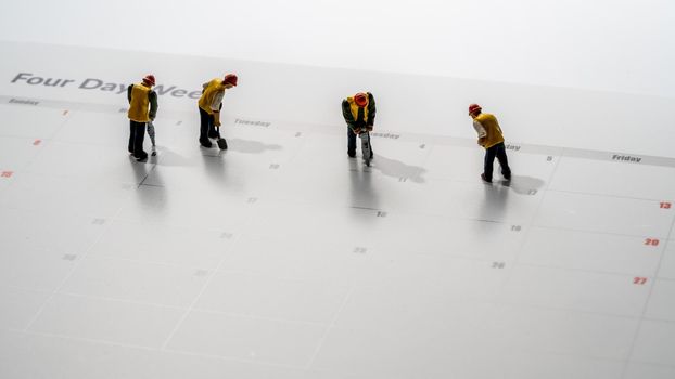 Printed calendar for a 4 day working week showing weekend days in red with small workmen working in the workweek