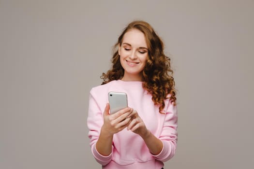 A happy young girl holding a phone looks into it and smiles.