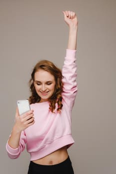 A happy young girl holds the phone looks into it and smiles holding her hand up.