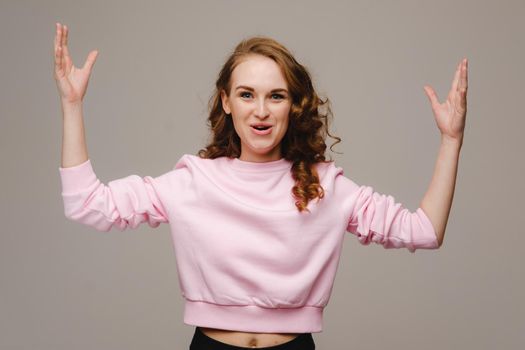 A beautiful girl on a gray background holds her head and screams emotionally.