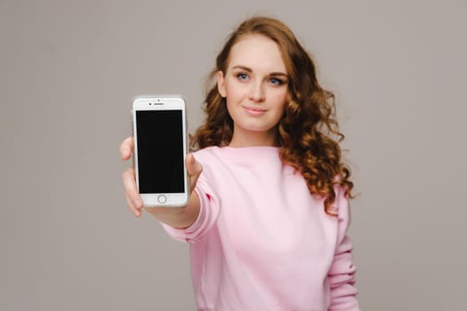 Fashionable girl with a smartphone on the background. Stands and shows the smartphone.