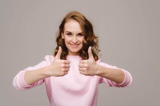 A beautiful girl on a gray background expresses her emotions and shows the sign everything is fine.