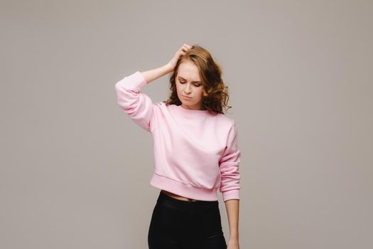 a girl with long hair on a gray background suffering from a headache holds her head with her hands. The girl puts her hands on her head, isolated against a gray background. The concept of problems and headaches
