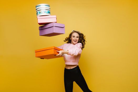 A happy young woman with colorful paper boxes after shopping isolated on an orange Studio background. Seasonal sales, purchases, spending money on gifts.